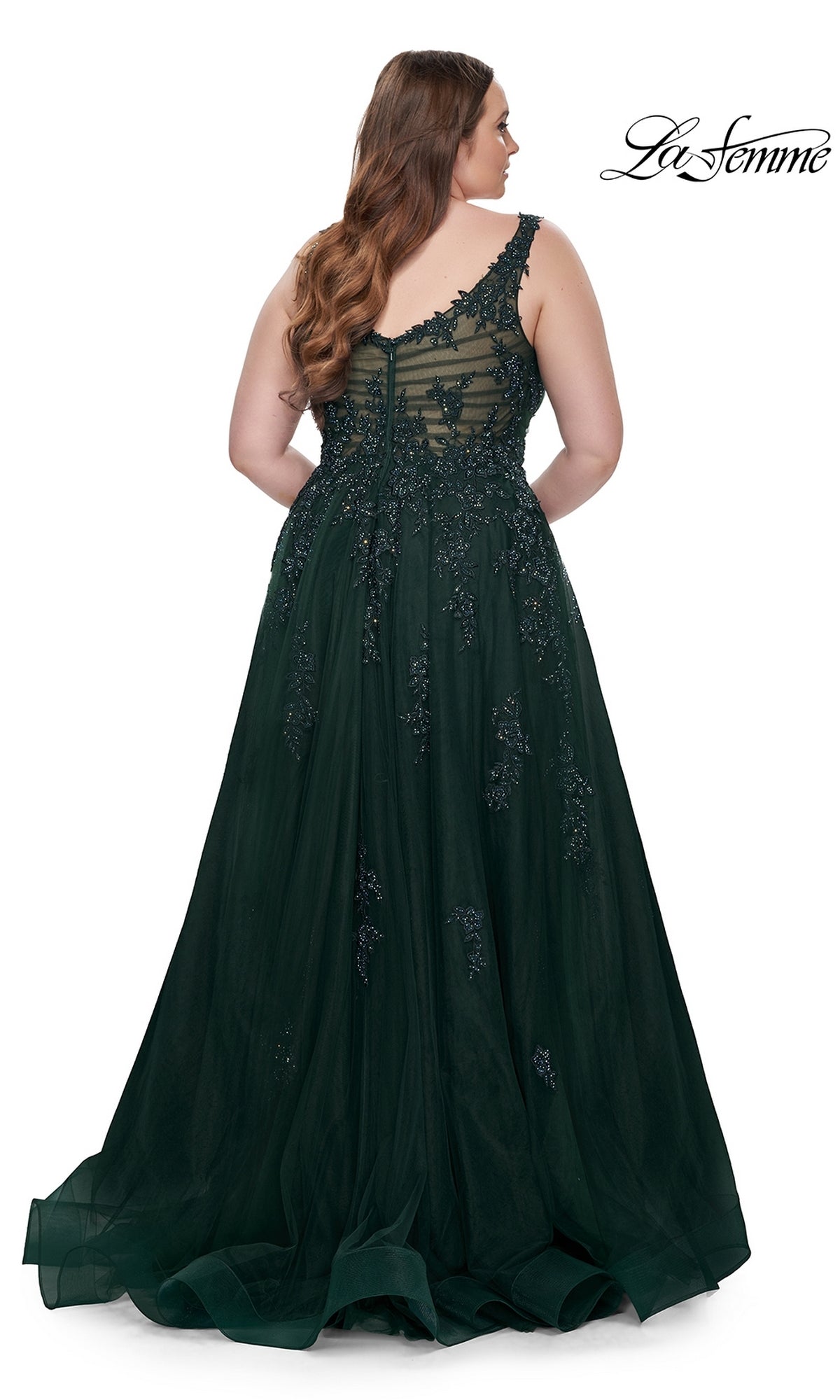 A woman faces away in the La Femme Long Prom Dress 31383—an embroidered dark green, floor-length lace gown with floral details and a sheer back. The La Femme logo appears in the top right corner.